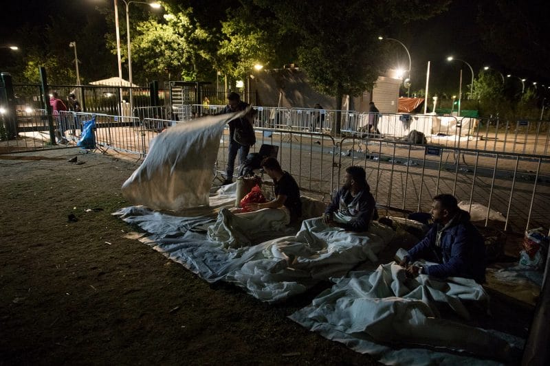 Vluchtelingen maken zich gereed om in de buitenlucht voor de hekken van het aanmeldcentrum te gaan slapen.